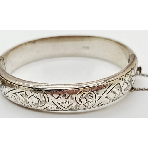 1033 - 2 vintage silver bangles, both with safety chains. A 12mm wide half brushed bangle with fern leaf de... 