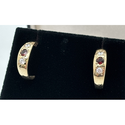 1007 - A pair of unmarked yellow gold gypsy style half hoop earrings, each set with a round cut garnet and ... 