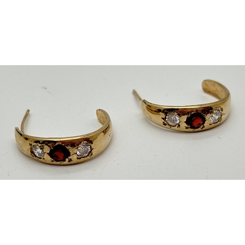 1007 - A pair of unmarked yellow gold gypsy style half hoop earrings, each set with a round cut garnet and ... 