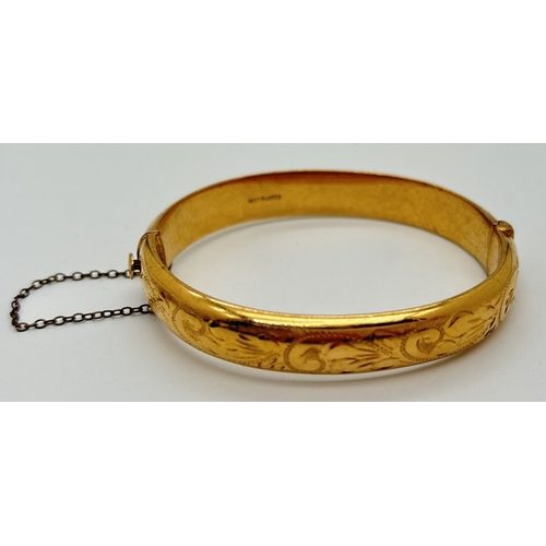 1053 - An 18ct gold plated bangle with push clasp, safety chain and half floral engraved decoration. Inside... 