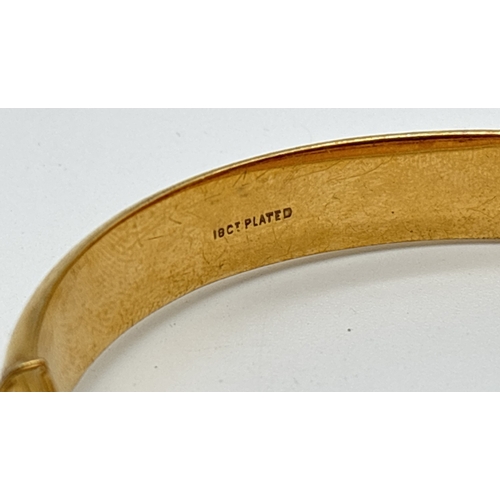 1053 - An 18ct gold plated bangle with push clasp, safety chain and half floral engraved decoration. Inside... 