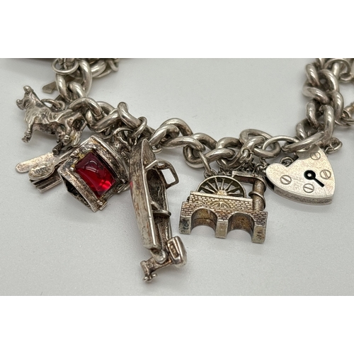 1084 - A vintage silver charm bracelet with safety chain and 15 silver and white metal charms, some with mo... 