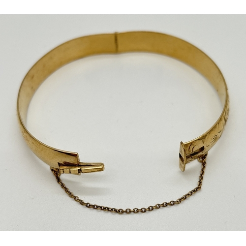 1093 - A 9ct rolled gold bangle with half floral decoration, push clasp and safety chain. Stamped marks to ... 