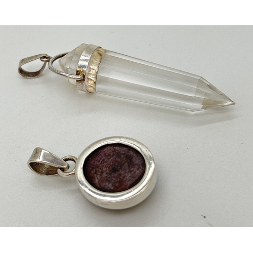 1098 - 2 small natural stone pendants. A circular shaped ruby cabochon pendant in a silver mount, together ... 