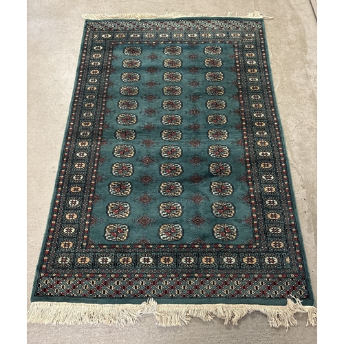 1475 - A vintage dark green ground rug with dark red, beige and pale blue colour design and tassled ends. A... 