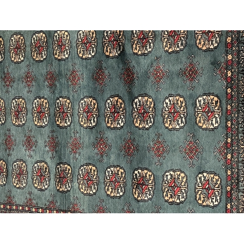 1475 - A vintage dark green ground rug with dark red, beige and pale blue colour design and tassled ends. A... 