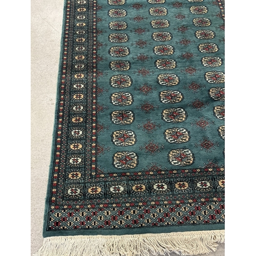 1475 - A vintage dark green ground rug with dark red, beige and pale blue colour design and tassled ends. A... 