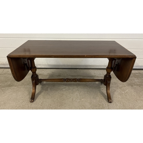 1489 - A vintage dark wood drop leaf coffee table with turned pedestal legs and stretcher. Sun fading to on... 