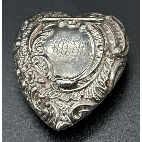 A Victorian silver heart shaped snuff box with decorative embossed detail of scroll & foliate design. Hinged circular shaped lid with engraved monogram. Hallmarked inside for Birmingham 1898. Approx. 5cm long x 4.25cm wide and weighs approx. 12.75g.