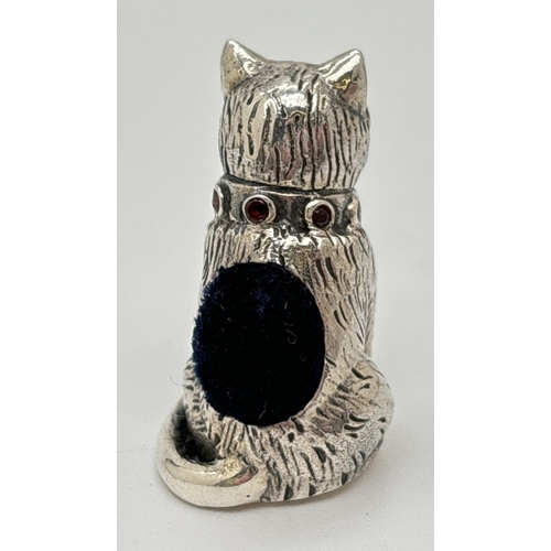 1174 - A miniature silver pin cushion modelled as a cat, with a collar of small round cut garnets and set w... 
