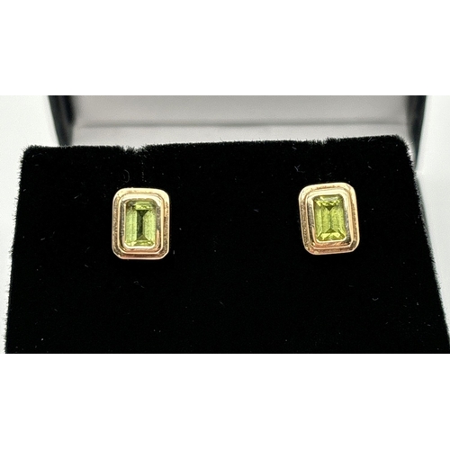 1061 - A pair of 9ct yellow gold square shaped stud earrings set with peridot stones. Earrings unmarked but... 