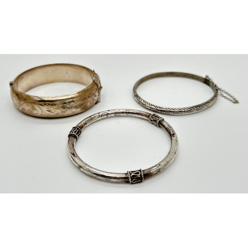 1076 - 3 silver and white metal bangles. A thin hinged bangle with diamond cut pattern and safety chain, a ... 