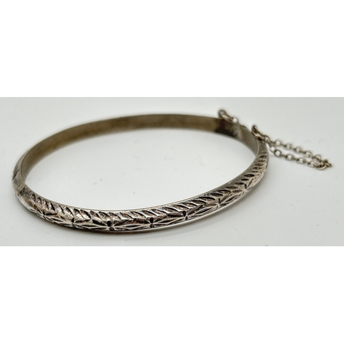 1076 - 3 silver and white metal bangles. A thin hinged bangle with diamond cut pattern and safety chain, a ... 