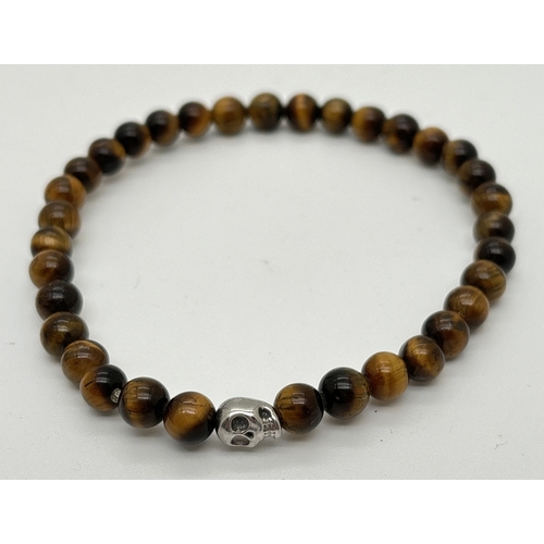 1102 - An unboxed tigers eye bracelet by Simon Carter, London. Small round tigers eye beads with a single s... 