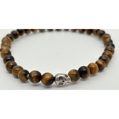 1102 - An unboxed tigers eye bracelet by Simon Carter, London. Small round tigers eye beads with a single s... 