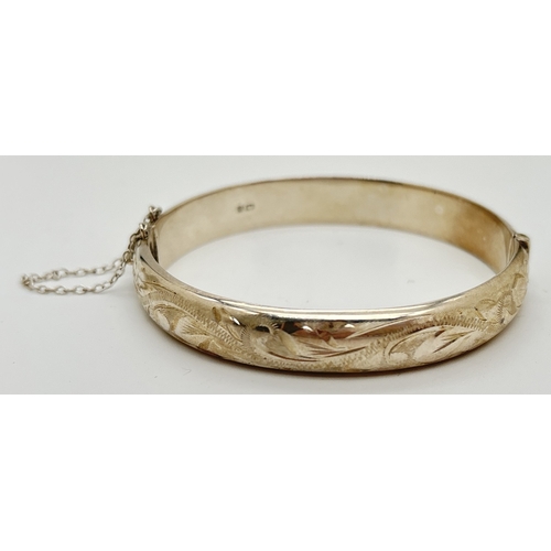 1115 - A silver hinged bangle with half floral engraved decoration and safety chain. Hallmarked Birmingham ... 