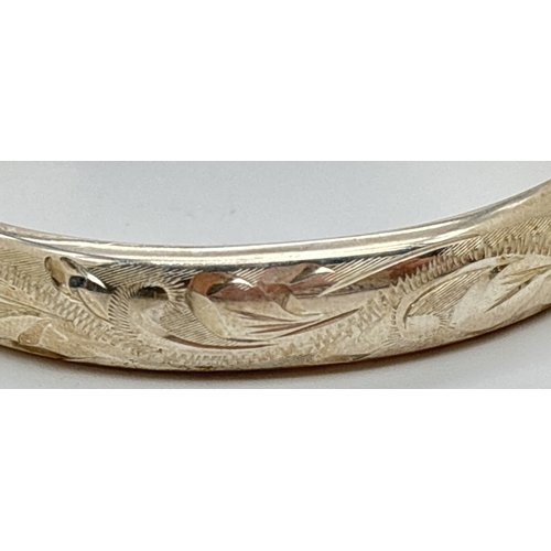 1115 - A silver hinged bangle with half floral engraved decoration and safety chain. Hallmarked Birmingham ... 