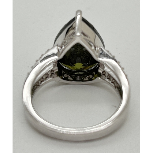 1095 - A Rhodium plated cocktail ring set with Swarovski crystals. A central single dark olive green pear c... 