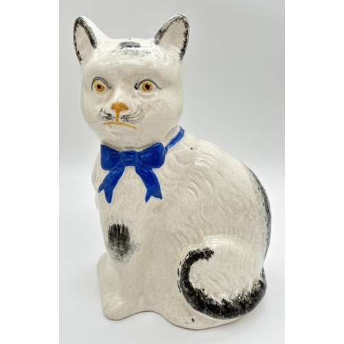 1230 - An antique Staffordshire pottery right facing white and black cat with blue bow to neck. White body ... 