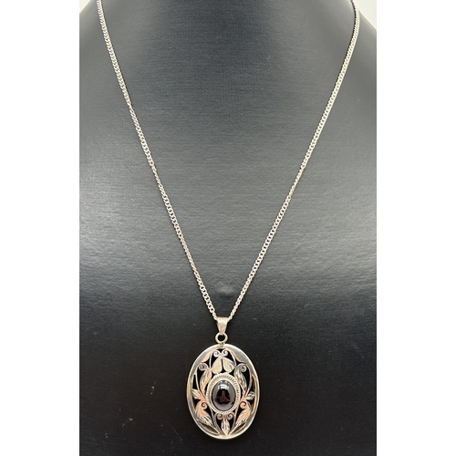 1026 - An oval shaped white metal pendant set with a central oval cut garnet cabochon. With pierced mount o... 