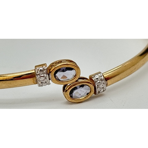 9 - A 9ct gold crossover style bangle with oval cut bezel set clear stone to each end. Hallmarked inside... 