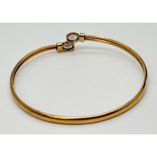 9 - A 9ct gold crossover style bangle with oval cut bezel set clear stone to each end. Hallmarked inside... 