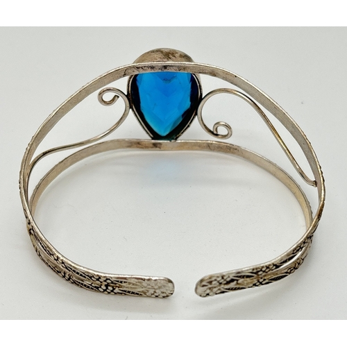 23 - A silver open work cuff style bangle with large blue pear cut central stone. With embossed floral de... 