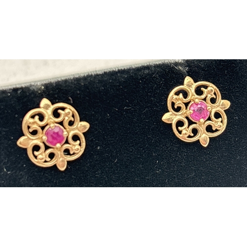 145 - A pair of yellow gold pierced design stud earrings each set with a small central round cut ruby. Wit... 