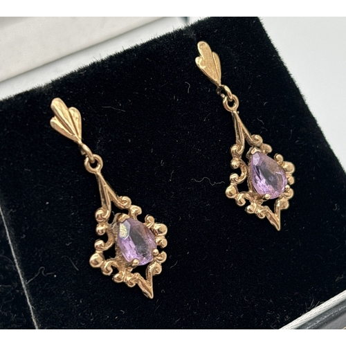  A pair of yellow gold drop style earrings with decorative mounts each set with an oval cut amethyst.... 