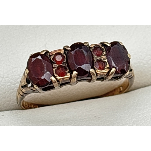 177 - A vintage 9ct gold, garnet set trilogy style ring with pierced work mount. Set with 3 oval cut garne... 