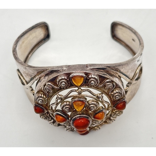 1013 - A large silver ethnic style cuff bangle with central pierced work design set with small pieces of ho... 