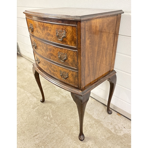 1377 - A small bow fronted walnut veneer 3 draw chest with decorative metal drop handles, raised on cabriol... 