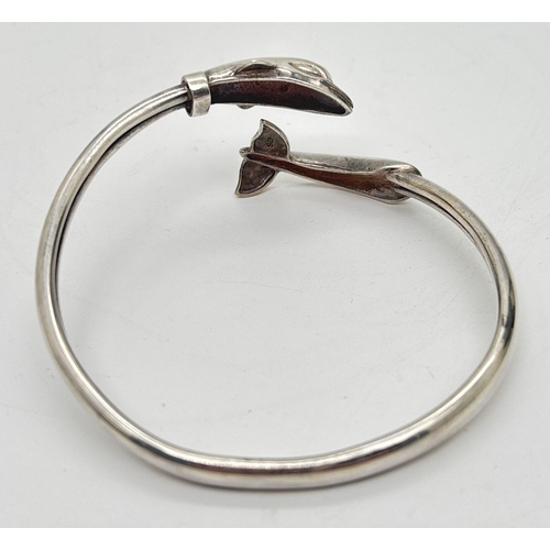 1046 - A 925 silver crossover style bangle with dolphin head and tail detail. Silver marks inside. Approx 1... 