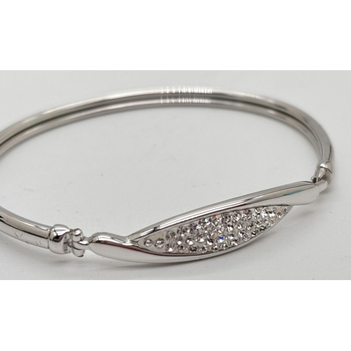 1052 - A boxed silver modern design bangle set with clear crystals in a crossover style panel. Hook and eye... 