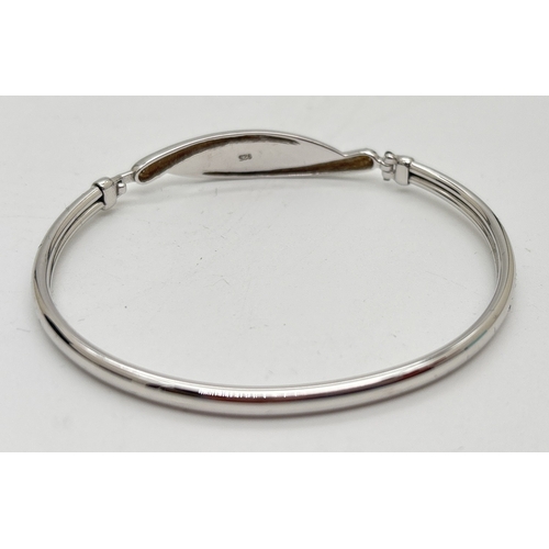 1052 - A boxed silver modern design bangle set with clear crystals in a crossover style panel. Hook and eye... 