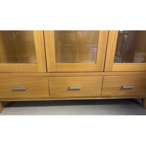 1384 - A modern light oak 2 door glass cabinet with fixed central glazed panel and 3 drawers. 2 glass shelv... 