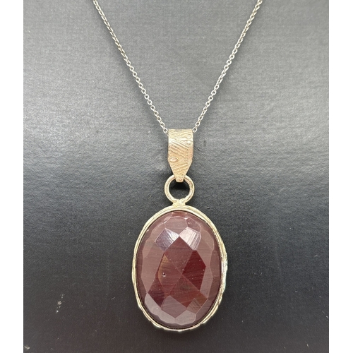 1075 - A boxed oval cut faceted garnet pendant in a decorative silver mount, on an 18