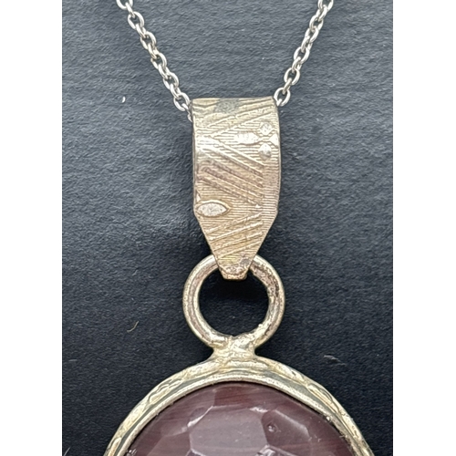 1075 - A boxed oval cut faceted garnet pendant in a decorative silver mount, on an 18