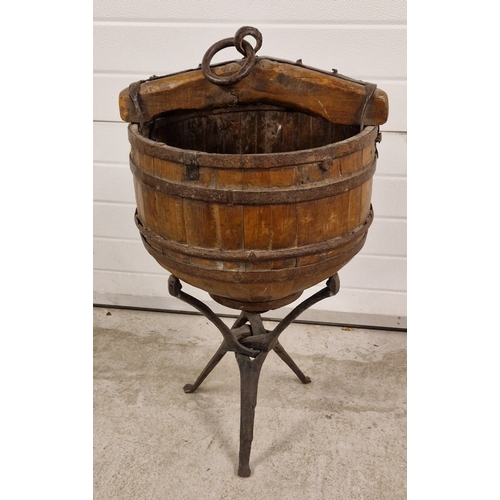 A late 19th century coopered Chinese well bucket with iron banding and hanging loop and curved base. Displayed on a rustic wooden tripod stand. Approx. 95cm tall on stand, bucket approx. 47cm diameter.