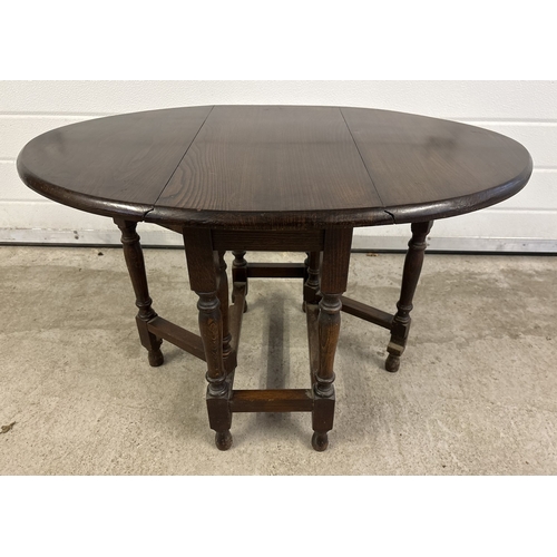 1378 - A small vintage dark oak, oval shaped low drop leaf table with turned legs. Approx. 48cm tall.