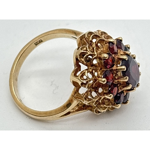 1107 - A vintage 9ct gold garnet set cluster style ring. High set filigree style mount with split shoulders... 