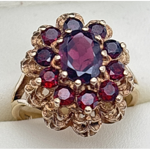 1107 - A vintage 9ct gold garnet set cluster style ring. High set filigree style mount with split shoulders... 