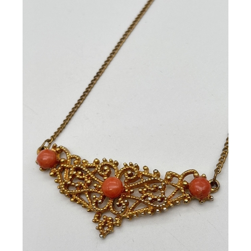 1125 - A vintage gold tone fixed pendant necklace with decorative pierced work detail, set with 3 coral cab... 