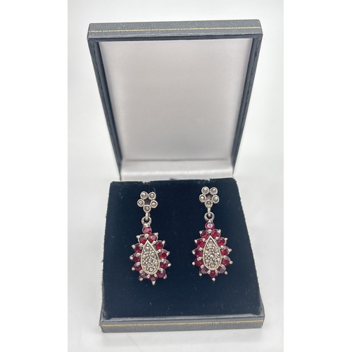 1007 - A pair of silver drop earrings each set with garnets and marcasite stones. Flower head design posts ... 