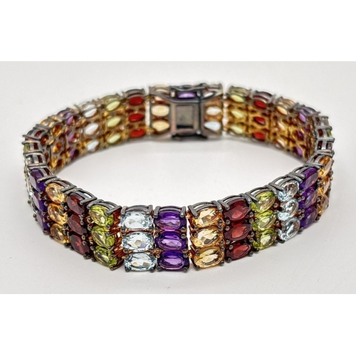 1002 - A decorative silver multi gemstone set tennis bracelet with push box clasp and safety clips. Set wit... 