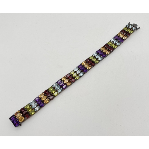 1002 - A decorative silver multi gemstone set tennis bracelet with push box clasp and safety clips. Set wit... 