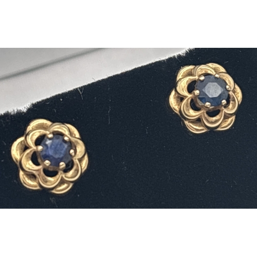 1009 - A pair of yellow gold and sapphire flower head design stud earrings. Each set with a central round c... 