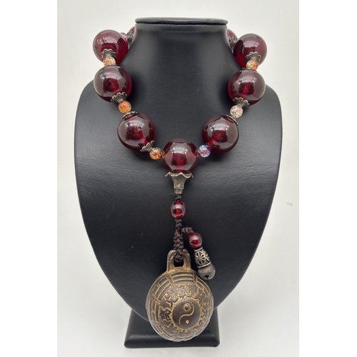 A Chinese exorcism or gossip bell on a string of large faux amber and ...