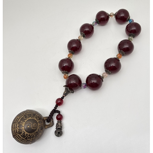 A Chinese exorcism or gossip bell on a string of large faux amber and ...