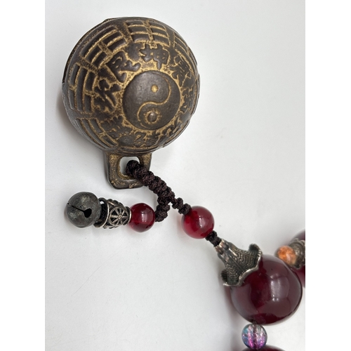 A Chinese exorcism or gossip bell on a string of large faux amber and ...